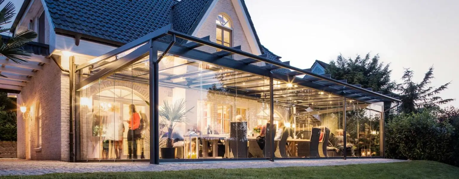 Moderne Wintergartenkonstruktion an einem hell beleuchteten Haus mit Menschen beim Essen