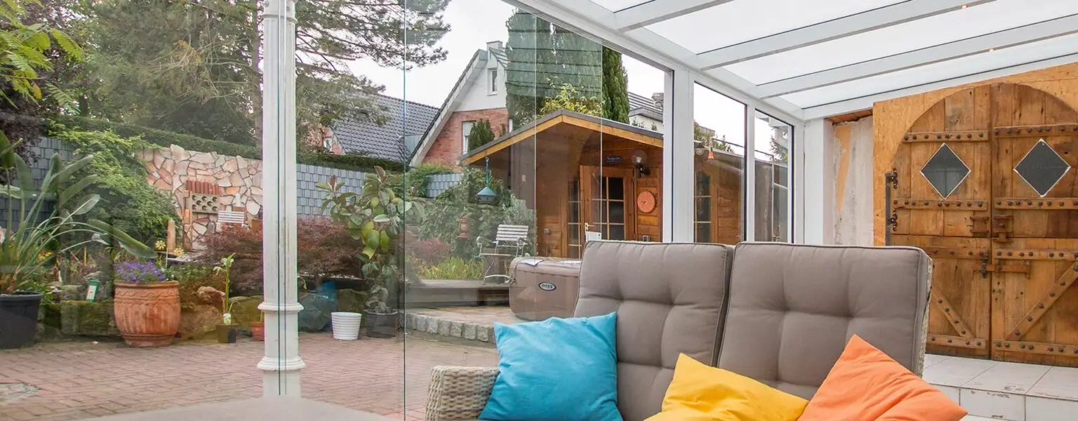 Helles Wohnzimmer mit Glasdach, bunten Kissen und Blick auf einen grünen Garten